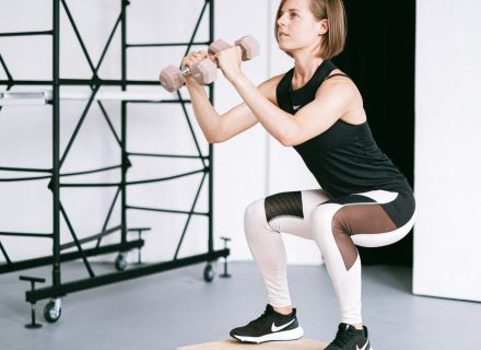 A woman in sportswear performs a squat with dumbbells indoors, embodying strength and healthy living.